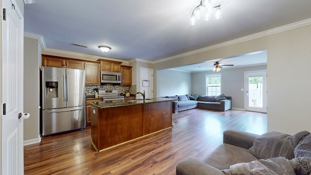 kitchen featuring dark wood-type flooring, a kitchen island with sink, decorative backsplash, stainless steel appliances, and ceiling fan