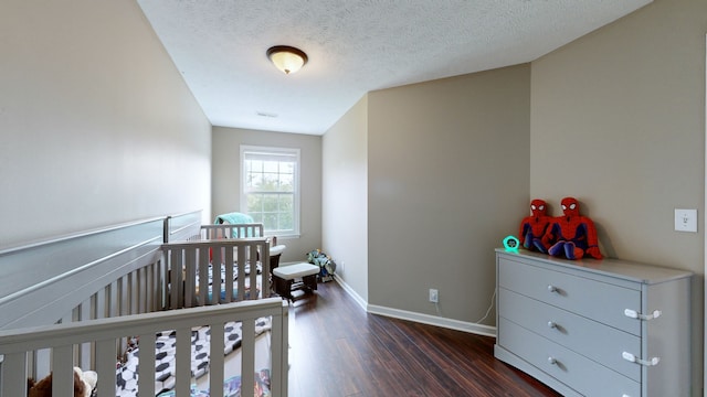 bedroom with a textured ceiling, a nursery area, and dark wood-type flooring