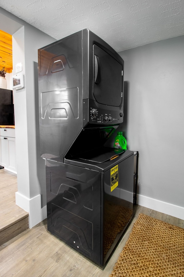 clothes washing area with stacked washer / dryer, a textured ceiling, and light hardwood / wood-style flooring