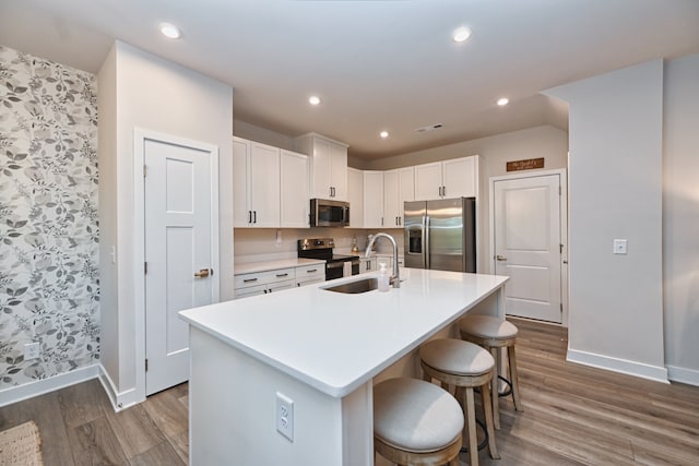 kitchen with sink, a center island with sink, white cabinetry, appliances with stainless steel finishes, and hardwood / wood-style floors