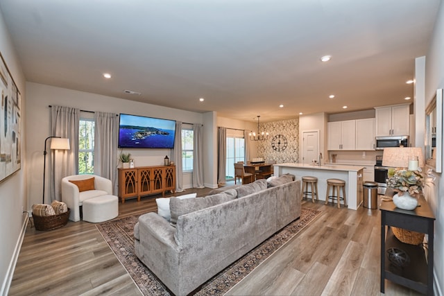 living room with an inviting chandelier, sink, and light hardwood / wood-style floors