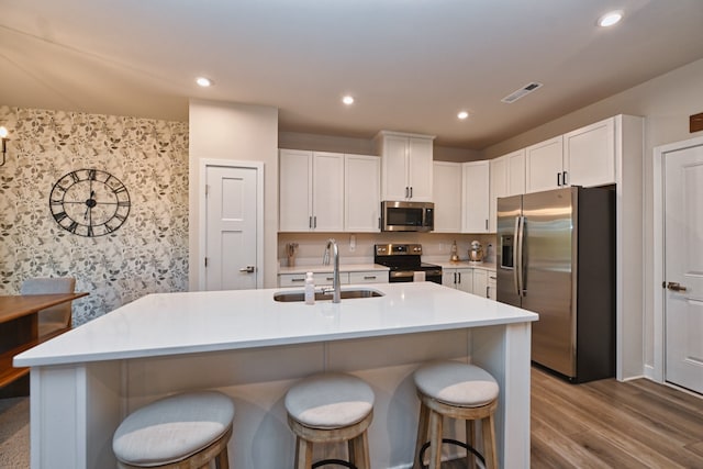 kitchen with appliances with stainless steel finishes, a kitchen island with sink, white cabinetry, and light hardwood / wood-style flooring