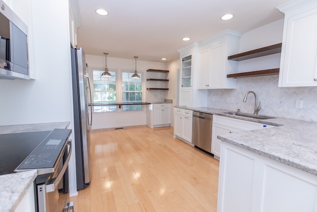 kitchen featuring appliances with stainless steel finishes, white cabinets, light wood-type flooring, decorative light fixtures, and sink