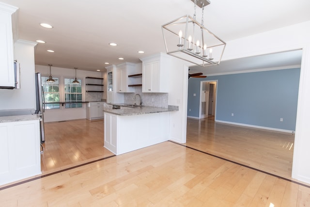 kitchen with light stone counters, white cabinets, light wood-type flooring, and sink