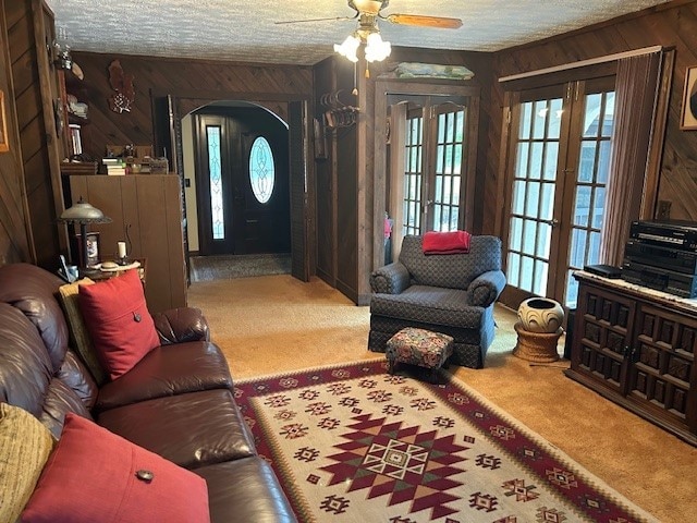 carpeted living room featuring french doors, a textured ceiling, wooden walls, and ceiling fan