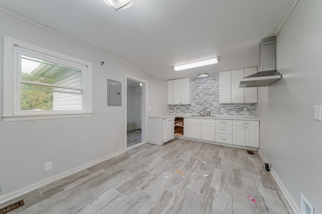 kitchen featuring electric panel, tasteful backsplash, wall chimney exhaust hood, white cabinetry, and light hardwood / wood-style floors