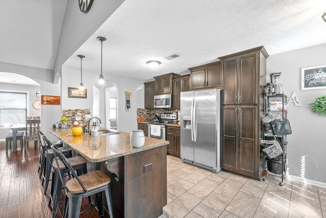 kitchen featuring dark brown cabinets, stainless steel appliances, decorative light fixtures, and light wood-type flooring