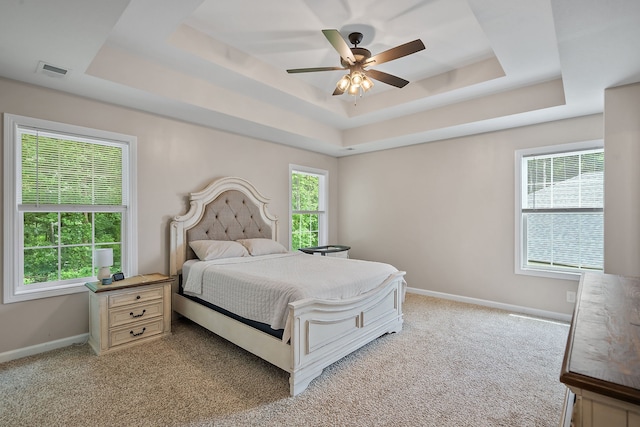 bedroom with ceiling fan, a raised ceiling, light carpet, and multiple windows