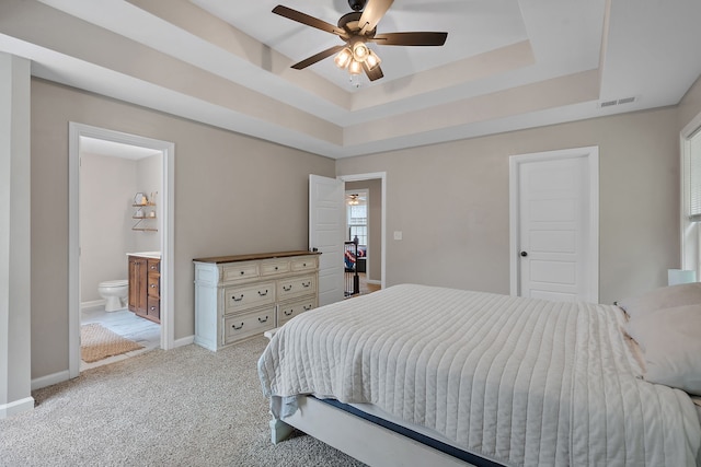 bedroom with a tray ceiling, ensuite bath, ceiling fan, and light colored carpet