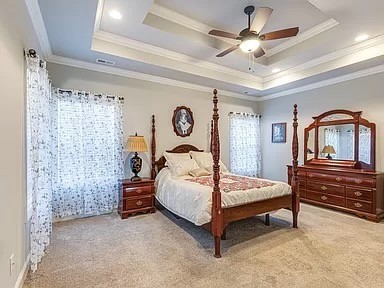 bedroom featuring ceiling fan, a tray ceiling, crown molding, and carpet flooring