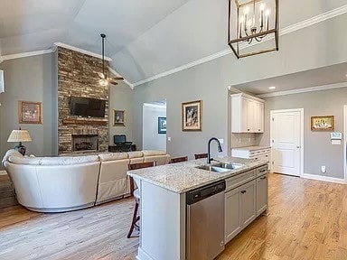 kitchen with an island with sink, sink, stainless steel dishwasher, light wood-type flooring, and vaulted ceiling