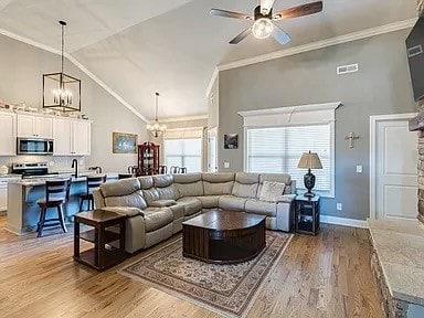 living room with ceiling fan with notable chandelier, light wood-type flooring, ornamental molding, and high vaulted ceiling