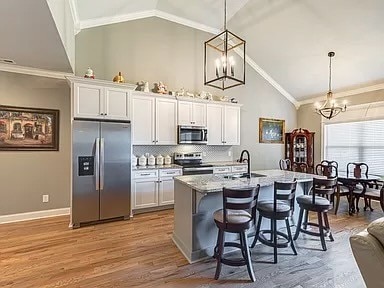 kitchen featuring stainless steel appliances, white cabinetry, vaulted ceiling, and hanging light fixtures