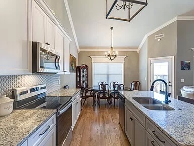 kitchen featuring stainless steel appliances, white cabinets, decorative light fixtures, and sink