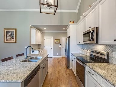 kitchen featuring sink, decorative light fixtures, white cabinetry, appliances with stainless steel finishes, and light wood-type flooring