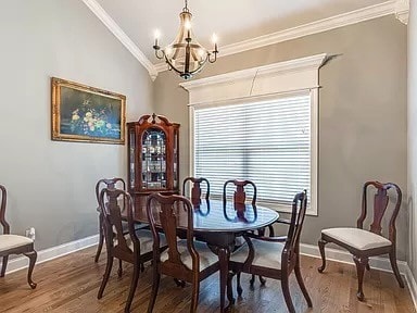 dining space with wood-type flooring, a chandelier, vaulted ceiling, and crown molding