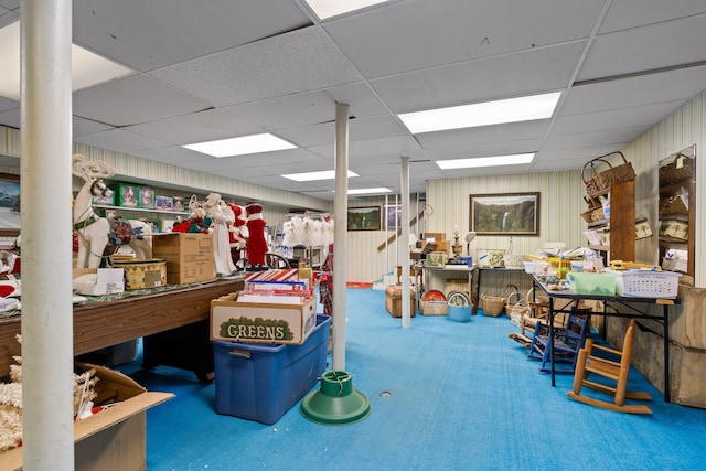 interior space with a paneled ceiling, wood walls, and carpet