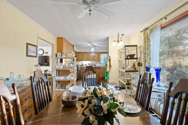 dining room with ornamental molding, wooden walls, and ceiling fan with notable chandelier