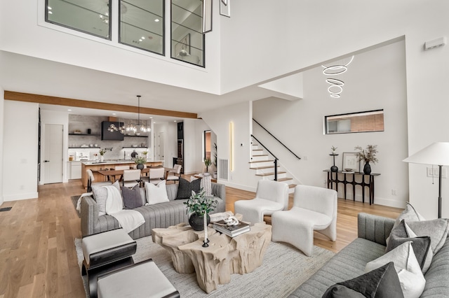 living room featuring light hardwood / wood-style flooring, a towering ceiling, and an inviting chandelier