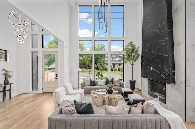 living room with light hardwood / wood-style floors, a high ceiling, an inviting chandelier, and a high end fireplace