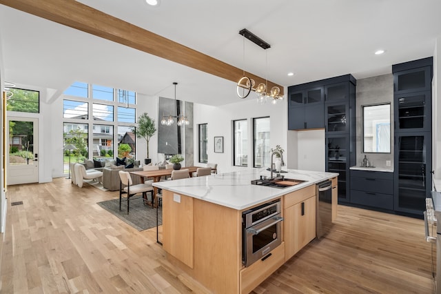 kitchen featuring pendant lighting, an island with sink, an inviting chandelier, stainless steel appliances, and light brown cabinetry