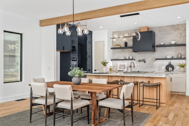 dining area with light hardwood / wood-style flooring, beam ceiling, and sink