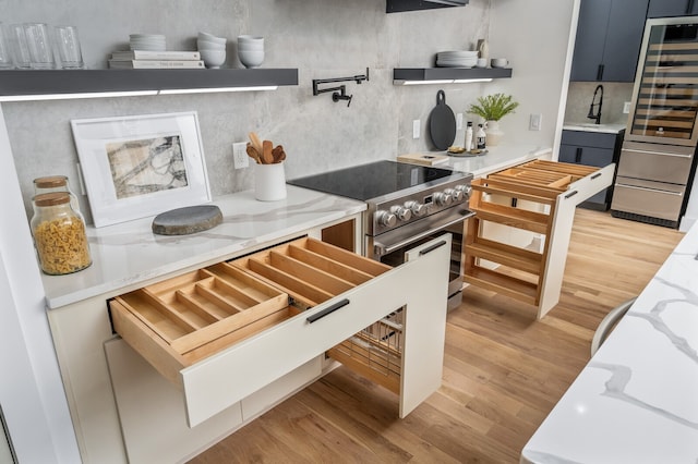 kitchen with high end stainless steel range, light stone countertops, light wood-type flooring, and sink