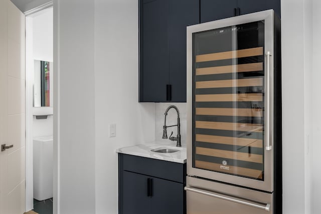 bar featuring tasteful backsplash, beverage cooler, sink, and light stone counters