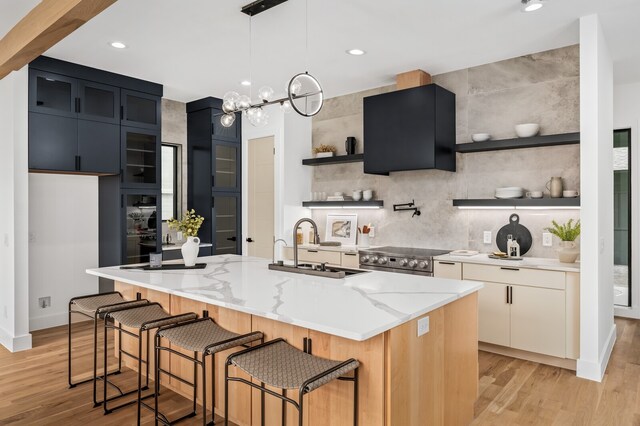 kitchen with light wood-type flooring, sink, a kitchen island with sink, electric stove, and light stone countertops