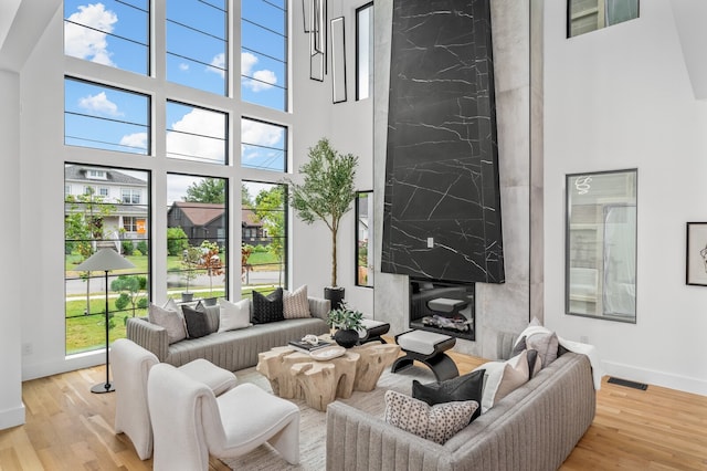 living room featuring a high ceiling, a fireplace, light hardwood / wood-style flooring, and a wealth of natural light