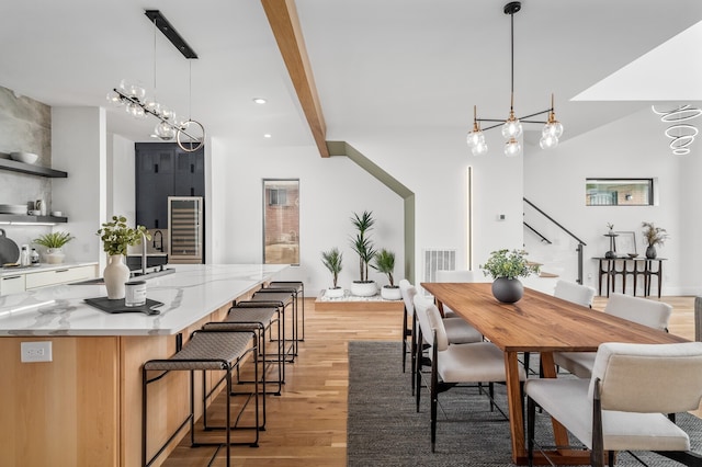 dining room with an inviting chandelier, light hardwood / wood-style flooring, sink, and beam ceiling