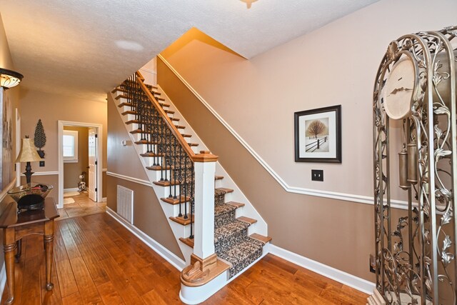 stairway with wood-type flooring and a textured ceiling