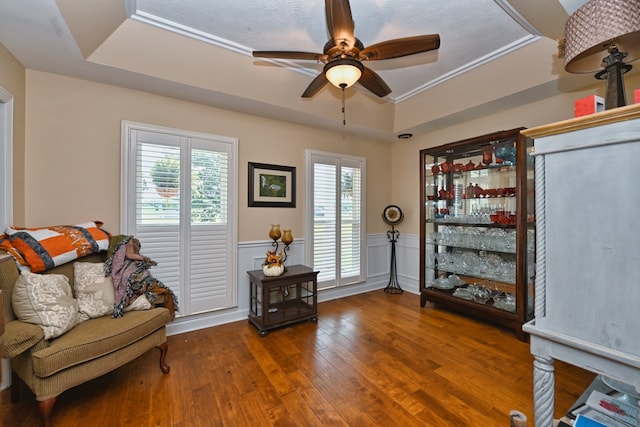 living area with wood-type flooring, a textured ceiling, a raised ceiling, ornamental molding, and ceiling fan