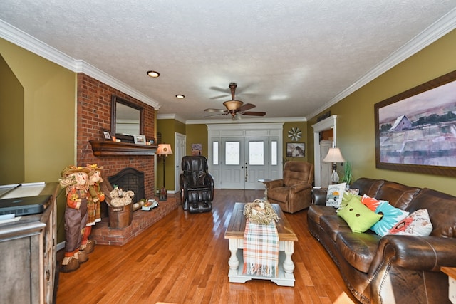 living room with light wood-type flooring, a textured ceiling, a brick fireplace, ornamental molding, and ceiling fan