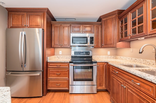 kitchen with light stone countertops, stainless steel appliances, light wood-type flooring, and sink