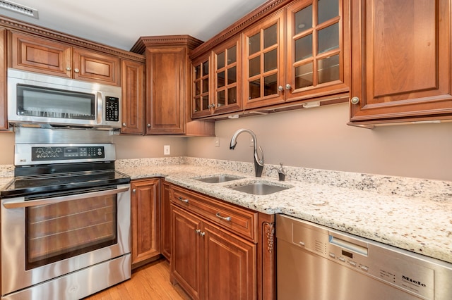 kitchen with light stone counters, light hardwood / wood-style floors, stainless steel appliances, and sink