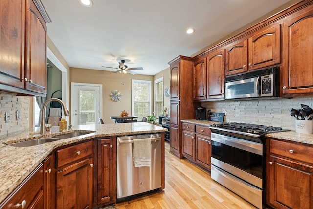 kitchen with ceiling fan, tasteful backsplash, light stone counters, light hardwood / wood-style flooring, and appliances with stainless steel finishes