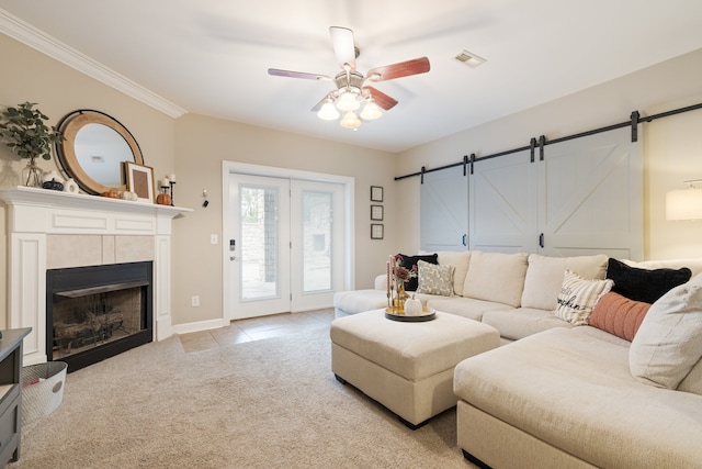 carpeted living room with a fireplace, a barn door, ceiling fan, and crown molding