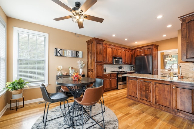 kitchen with decorative backsplash, light stone counters, stainless steel appliances, and light hardwood / wood-style floors