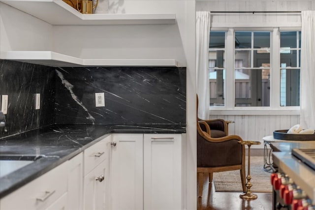 kitchen featuring backsplash, dark stone countertops, white cabinetry, and wooden walls