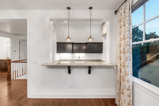 kitchen with light stone countertops, a breakfast bar, pendant lighting, and dark hardwood / wood-style floors