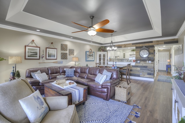 living room featuring ceiling fan with notable chandelier, hardwood / wood-style flooring, a tray ceiling, and crown molding