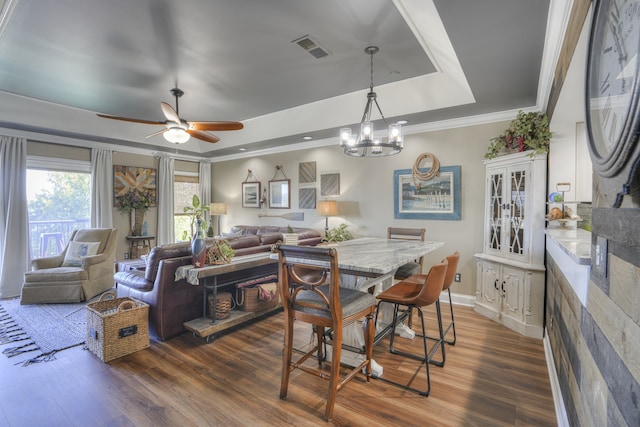 dining area featuring ceiling fan with notable chandelier, crown molding, dark hardwood / wood-style floors, and a raised ceiling