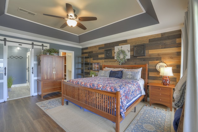 bedroom featuring wooden walls, ceiling fan, dark hardwood / wood-style floors, a tray ceiling, and a barn door