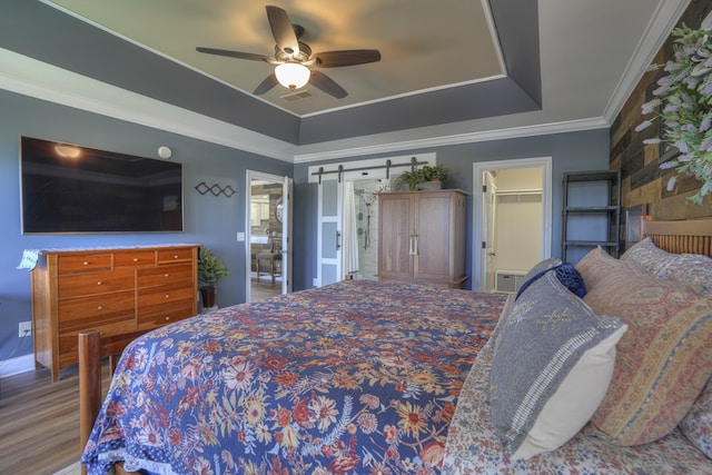 bedroom featuring a spacious closet, ceiling fan, a closet, wood-type flooring, and a barn door