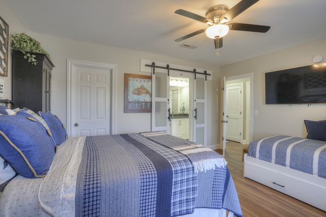 bedroom featuring a barn door, dark hardwood / wood-style floors, ensuite bathroom, and ceiling fan