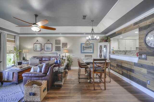 dining area featuring ceiling fan with notable chandelier, a raised ceiling, dark hardwood / wood-style floors, and ornamental molding