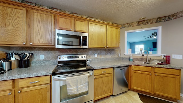 kitchen with appliances with stainless steel finishes, backsplash, a textured ceiling, ceiling fan, and sink