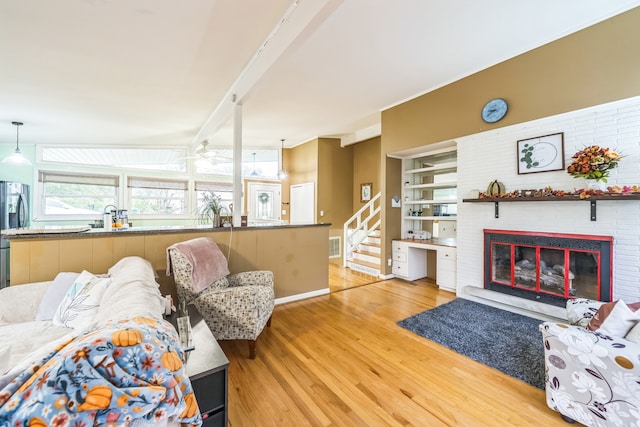 living room featuring a brick fireplace, hardwood / wood-style flooring, beam ceiling, and ceiling fan