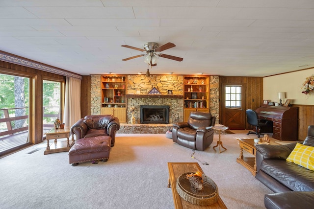 living room with built in shelves, ceiling fan, carpet floors, and a stone fireplace